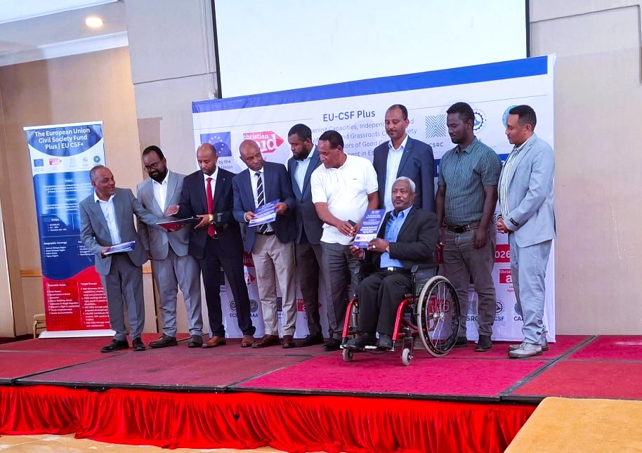People stand on a stage at a disability partnership event; one participant uses a wheelchair.
